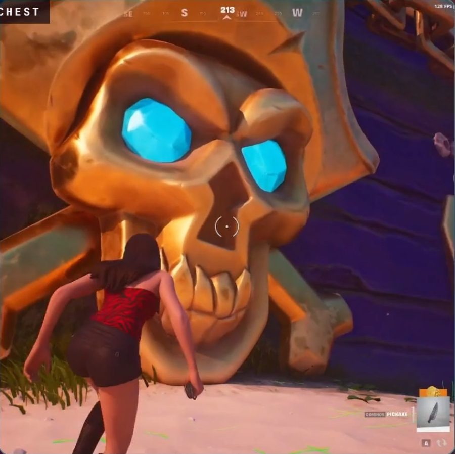 A player standing on the sand in front of the pirate chest's huge golden skull and crossbones, which has glowing blue gem eyes.